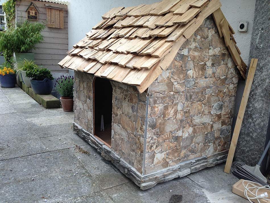 Hundehütte mit Schindeldach und Wand aus Bruchstein