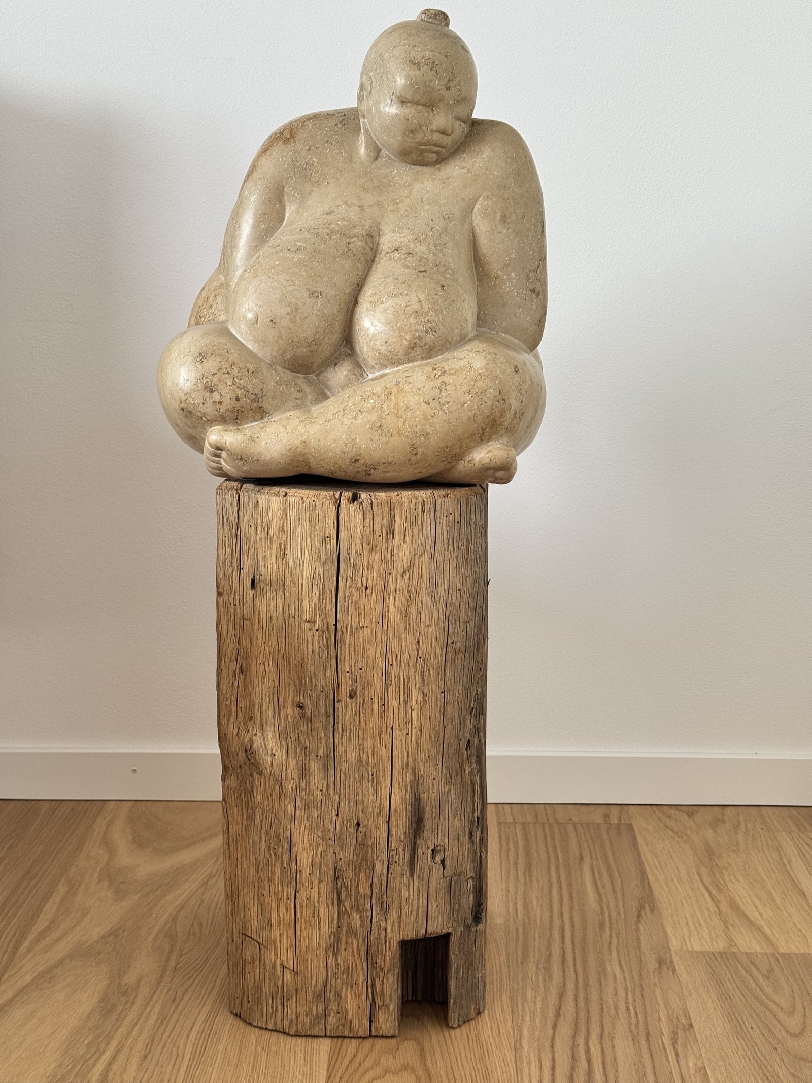 Holzskulptur einer sitzenden Figur auf einem Baumstumpf